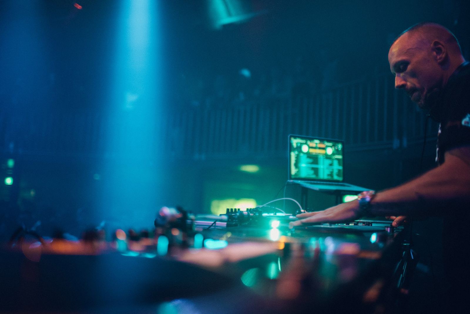 DJ Revolution cutting on turntables under teal club lights